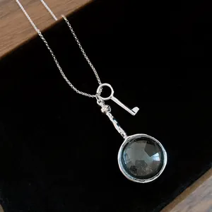 Close-up of vintage silver magnifying glass and key pendant on black velvet surface.