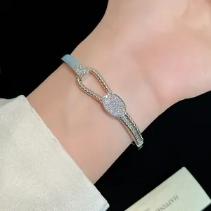 Detailaufnahme eines 18K vergoldeten geflochtenen Armreifs mit Zirkonia-Knoten am Handgelenk