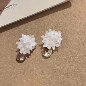Detailaufnahme von eleganten weißen Resina-Blumenohrringen mit klaren Tropfenanhängern.
