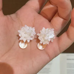 Nahaufnahme von eleganten weißen Harzblumen-Ohrringen mit einem durchsichtigen Tropfenanhänger