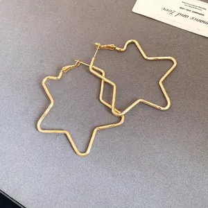 Detailed view of oversized 18k gold plated star hoop earrings on a grey background.