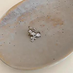 Primo piano di un ear cuff in argento e zirconi con ciondolo a croce su un piatto di ceramica