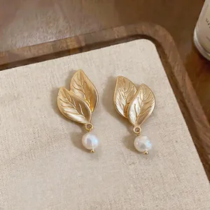 Vista macro detallada de elegantes pendientes de hoja dorada con perlas de agua dulce