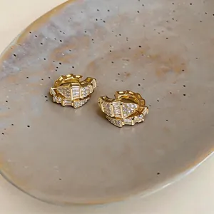 Primo piano di ear cuff placcati in oro con zirconi brillanti su un piatto in ceramica