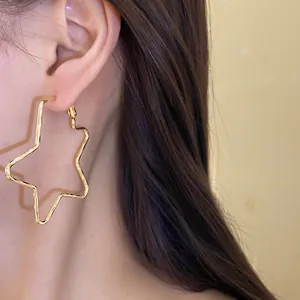 Detail view showing oversized 18k gold plated star-shaped hoop earrings worn on the ear