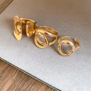Detail of gold hollow rings with cross-wrap and minimalist oval designs on grey board