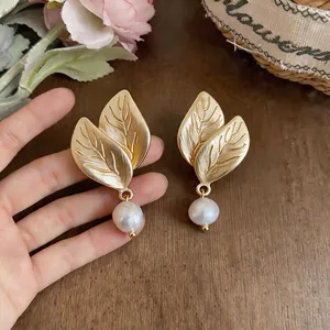 Primer plano de elegantes pendientes de hoja dorada estilo francés con perlas blancas.