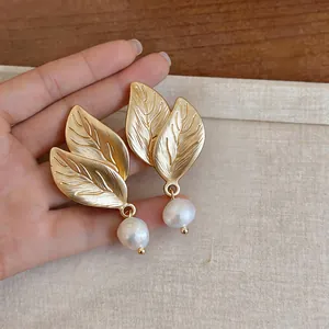 Primer plano de elegantes pendientes de hoja dorada con perlas de agua dulce.