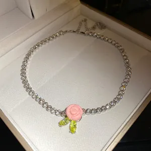 Close-up of elegant tennis necklace with pink resin rose and green zircon leaves
