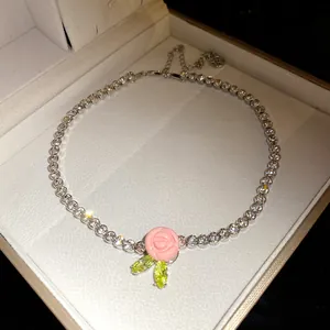 Detailed view of the pink resin rose pendant with green zircon leaves on a tennis chain