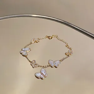 Detailansicht eines goldfarbenen Armbands mit funkelnden Zirkon- und Muschel-Schmetterlingen.