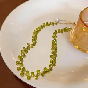 Close-up of green beaded necklace with gold chain and pearl on a white ceramic plate.