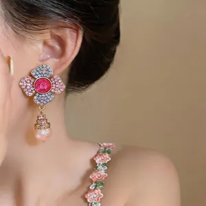 Close-up of floral rhinestone stud earrings with hanging pearl pendant on ear