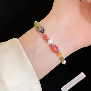 Close-up detail of a colorful beaded stone and pearl bracelet on a feminine wrist.