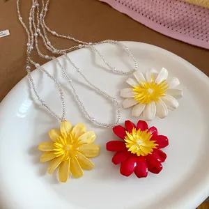 Gros plan de pendentifs marguerites colorés sur des colliers de perles blanc, jaune et rouge