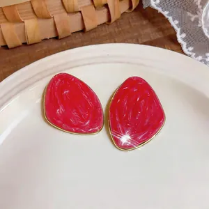 Primo piano di orecchini a lobo geometrici irregolari in smalto rosso con bordi dorati.