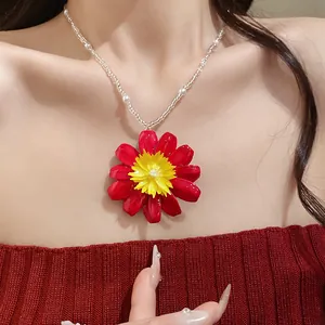 Détail d'un pendentif marguerite rouge et jaune sur un collier de perles blanches délicates