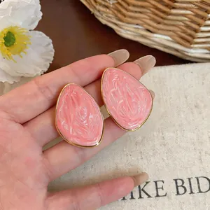 Primo piano di orecchini a perno geometrici irregolari rosa con bordi dorati.