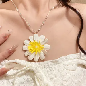 Détail d'un collier pendentif marguerite blanche avec perles sur un mannequin en dentelle