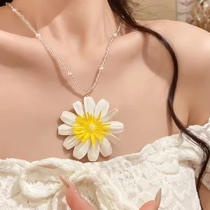 Gros plan d'un pendentif marguerite blanche et jaune sur un collier de perles sucrées