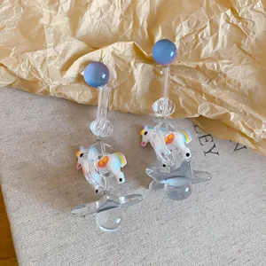 Playful carousel horse and star resin drop earrings with blue gradient orbs.