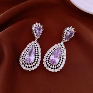 Close-up detail of luxurious purple teardrop zircon hollow drop earrings on brown fabric