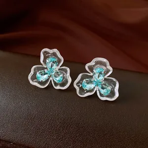 Close-up of light blue zircon flower stud earrings with transparent petals on brown leather.