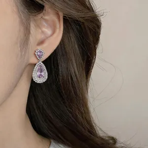 Close-up of elegant purple teardrop earrings with shimmering zircon accents on model.