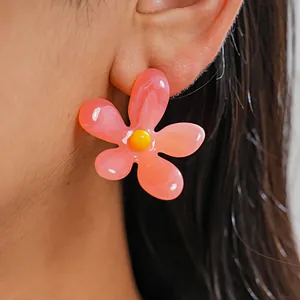 Close-up of a vibrant pink resin flower earring with a yellow center on a model's ear