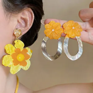 Detailed view of oversized orange and yellow resin flower drop earrings on model