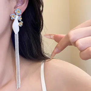 Gros plan de boucles d'oreilles fleurs émaillées vintage avec de longs pompons argentés