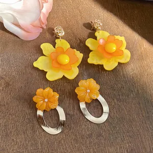Close-up of yellow and orange resin flower earrings with gold oval hoop details