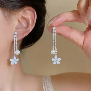 Detail view of elegant dangling earrings with zircons, pearls, and white resin flowers.