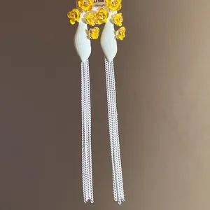 Détail de boucles d'oreilles vintage avec fleurs jaunes et longs glands argentés.