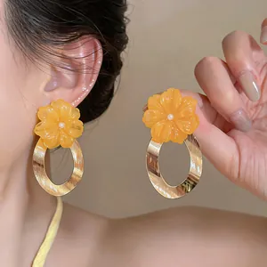 Detailed macro view of orange resin flower earrings featuring large metallic gold oval hoops