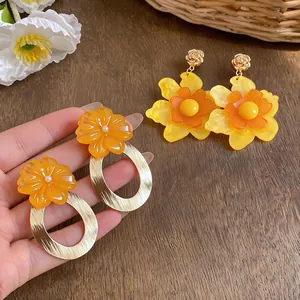 Close-up of vibrant orange resin flower earrings with elegant textured gold metal hoops.