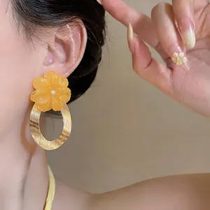 Detailed close-up of yellow resin flower earrings with brushed gold oval pendant drops