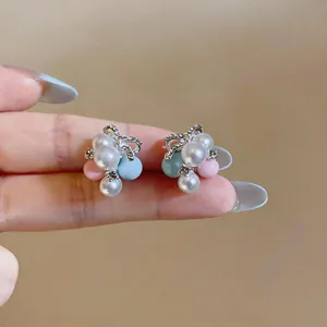 Close-up detail of silver needle stud earrings with macaron pearls and rhinestone bow