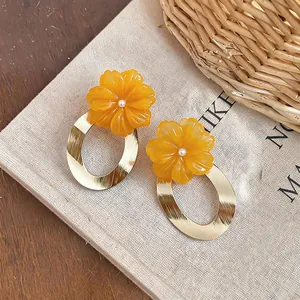 Close-up of elegant resin orange flower earrings with gold-finished oval rings
