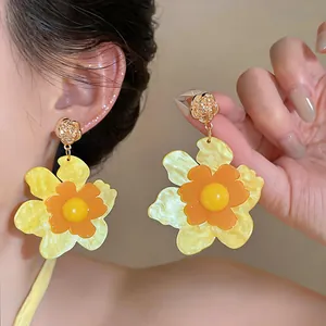 Macro view of exaggerated resin flower drop earrings with layered yellow and orange petals.