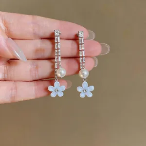 Detailed view of silver drop earrings with zircon, pearl, and blue resin flower charm