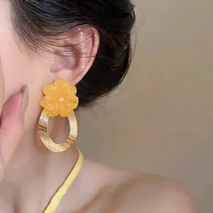 Close-up of elegant orange resin flower earrings with textured gold hoop on an Asian model