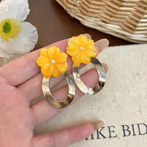 Detailed view of yellow resin flower earrings with gold brushed oval hoops.