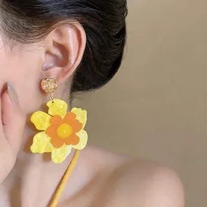 Detailed macro view showing vibrant yellow and orange resin flower drop earrings on model