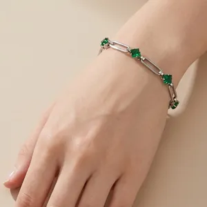 Detail view of a stainless steel paperclip bracelet with green rhombus crystals on a wrist.