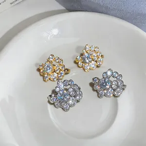Close-up of delicate floral round zircon ear clips in gold and silver on a white plate.