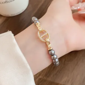 Detailansicht eines grauen Perlenarmbands mit goldenem Schweinenasenverschluss