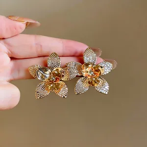 Primo piano di eleganti orecchini a lobo a fiore dorati con accenti di cristallo brillante
