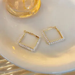 Makrodetail der geometrischen Rautenohrringe mit klaren Glasperlen auf Golddraht.