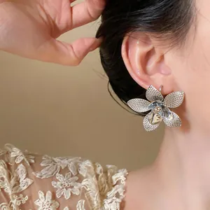 Primo piano di un orecchino a lobo a forma di fiore in metallo argento su un orecchio di modella